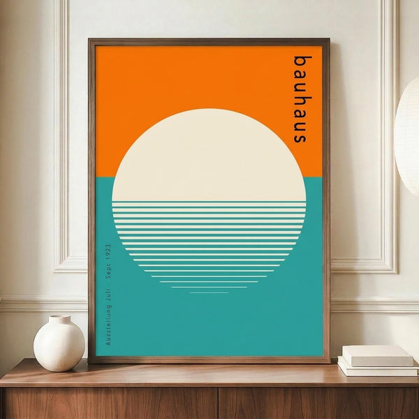 May include: Framed Bauhaus-style poster with geometric design featuring large cream circle against orange and teal color blocks, white horizontal lines creating reflection effect, displayed on wooden credenza beside white ceramic vase and stacked books in elegant room with white paneled walls.