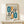 May include: Bauhaus-style poster print in light wood frame displaying abstract geometric shapes in teal and orange with black lines and concentric rectangles, displayed on white wooden console table next to small wrapped gift with botanical sprig against cream wall
