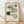 May include: Framed geometric art print with curved flowing lines in black and green on cream background, displayed in light wood frame against white wall on wooden floor with soft natural lighting and fabric shadows
