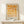 May include: Framed geometric art print with orange and yellow circular and semi-circular shapes arranged in a grid pattern, displayed on a light wood console table against a cream wall. The poster features "BAUHAUS 1923" text at bottom and gradual color transition from deep orange at top to pale yellow at bottom. Small wrapped gift box sits beside the natural wood frame.