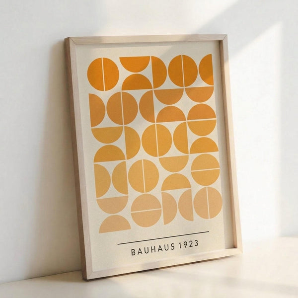 May include: Framed geometric art print featuring orange and yellow circles and semicircles arranged in a grid pattern on cream background, displayed in light wood frame leaning against white wall with soft natural lighting creating shadows