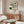 May include: Minimalist room with wooden sideboard displaying framed geometric art print featuring green circles and black line patterns on cream background, accompanied by white sculptural chair, glass coffee table, and modern lamp in neutral-toned interior setting.