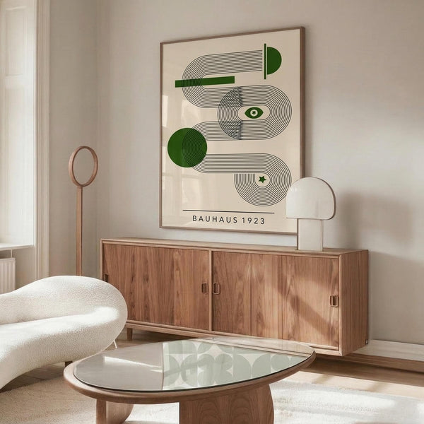 May include: Minimalist room with wooden sideboard displaying framed geometric art print featuring green circles and black line patterns on cream background, accompanied by white sculptural chair, glass coffee table, and modern lamp in neutral-toned interior setting.
