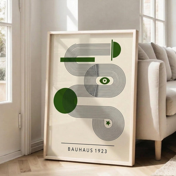 May include: Framed geometric art print featuring abstract curved lines in black and green on cream background, displayed in light wooden frame leaning against white wall next to beige sofa in bright living room with large windows and natural lighting.