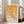 May include: Framed geometric art print with orange and yellow circles and semicircles arranged in a grid pattern on cream background, displayed on hardwood floor next to beige upholstered sofa in bright living room with white walls and large windows.
