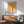 May include: Framed geometric poster with orange and cream circles and semicircles in grid pattern, displayed above wooden sideboard with table lamp. Mid-century modern living room setting features sage green upholstered armchair with wooden frame, round coffee table, and natural sunlight casting shadows on white wall.