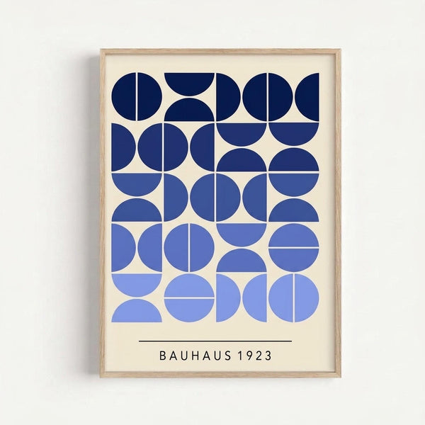 Framed geometric art print featuring various blue circles, semicircles, and quarter circles arranged in a grid pattern on cream background. The design uses gradient shades from navy to light blue, with clean lines dividing the circular shapes. Text reads "BAUHAUS 1923" at bottom. Natural wood frame hangs on white wall.