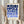 May include: Person holding framed geometric poster with blue circles and semicircles in gradient shades from navy to light blue on cream background, text reading "BAUHAUS 1923" below design. Light wood frame, neutral wall backdrop, dried pampas grass visible on left side.