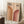 May include: Framed Bauhaus poster with geometric rainbow arcs in warm orange and burgundy tones on beige background, displaying "BAUHAUS 1923" text. Poster leans against white wall corner next to wooden side table with white coffee cup, cream textured rug, and beige knit throw blanket creating cozy modern interior styling.