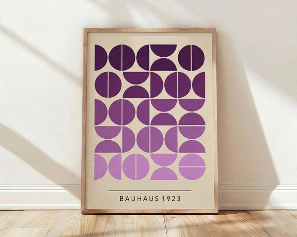 May include: Framed geometric art print with purple and lavender circles and semicircles arranged in a grid pattern on cream background, displayed in light wood frame against white wall on wooden floor with natural lighting creating soft shadows
