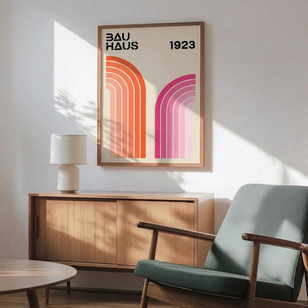 May include: Framed Bauhaus poster with orange and pink geometric curved stripes on cream background, displayed above mid-century modern wooden credenza with table lamp, next to sage green upholstered armchair with wooden arms in sunlit room with white walls