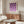 May include: Purple and lavender geometric circles poster in wood frame above walnut sideboard in modern living room. White curved chair and glass coffee table visible. Cream walls with natural lighting. Poster features semicircles and quarter-circles in gradient purple tones on cream background with Bauhaus 1923 text.