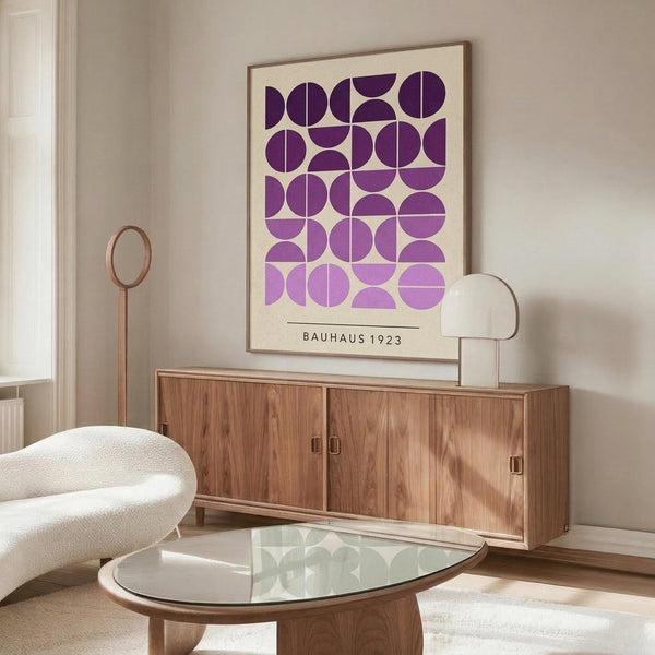 May include: Purple and lavender geometric circles poster in wood frame above walnut sideboard in modern living room. White curved chair and glass coffee table visible. Cream walls with natural lighting. Poster features semicircles and quarter-circles in gradient purple tones on cream background with Bauhaus 1923 text.