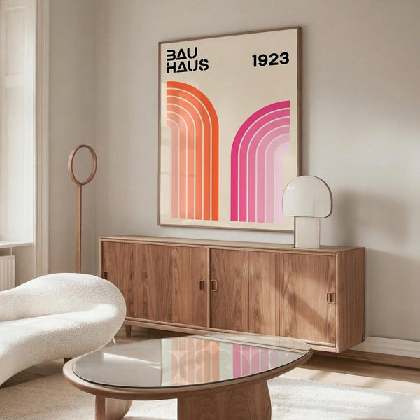 May include: Modern living room with Bauhaus-inspired poster featuring orange and pink curved geometric shapes and "1923" text, displayed above walnut sideboard. White sculptural chair and glass coffee table complete the mid-century modern setting with neutral walls and natural lighting.