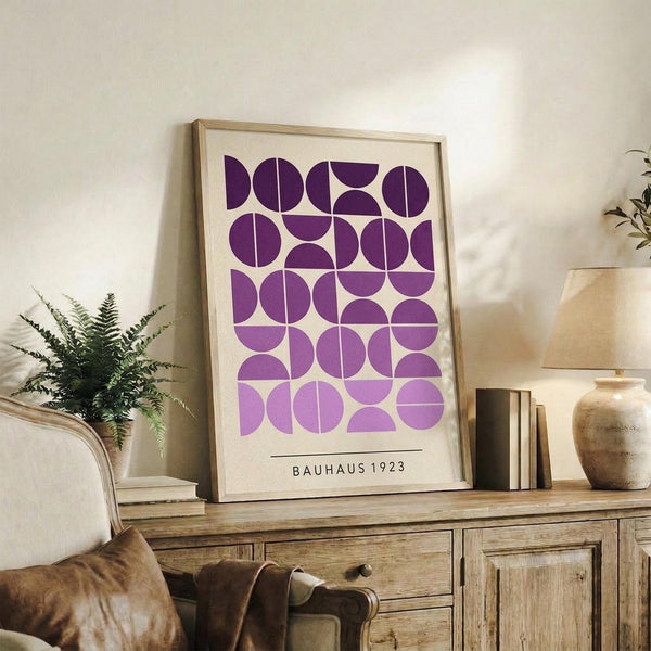 May include: Framed geometric poster with purple circles and semicircles in a grid pattern on cream background, displayed on rustic wooden sideboard next to fern plant, ceramic vases, and books in neutral living room setting