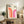 May include: Framed Bauhaus poster with geometric rainbow arcs in orange and pink gradients, displayed on rustic wood sideboard with books, ceramic vases, and fern plant in neutral-toned living room setting with beige chair and textured throw pillows