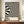 May include: Black and cream wavy striped abstract poster with "BAUHAUS" text in wooden frame, displayed on walnut sideboard next to white ceramic vase and stacked books against beige wainscoted wall in modern interior setting.