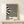 May include: Black and cream wavy striped abstract poster in wooden frame, displayed on light wood surface against beige wall. Small white wrapped gift with greenery sits beside frame. Bold geometric pattern creates optical illusion effect with flowing, distorted lines throughout design.