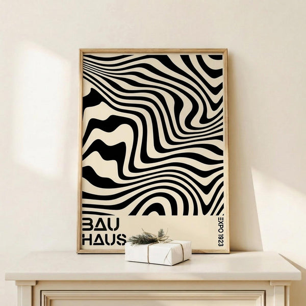 May include: Black and cream wavy striped abstract poster in wooden frame, displayed on light wood surface against beige wall. Small white wrapped gift with greenery sits beside frame. Bold geometric pattern creates optical illusion effect with flowing, distorted lines throughout design.