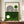 May include: Framed Bauhaus-style poster with geometric black line art forming curved shapes on cream and green color-blocked background, displayed on wooden sideboard next to white ceramic vase and stacked books in modern interior with white paneled walls.
