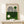 May include: Framed Bauhaus-style poster with geometric design featuring black concentric lines forming arch and circle shapes, green and cream color blocks, dark green circle, displayed on light wood surface next to small wrapped gift with twine and evergreen sprig against cream wall.