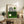 May include: Framed Bauhaus-style poster with geometric black line design and green circle on cream background, displayed on rustic wooden sideboard with books, ceramic vase, and fern plant in modern living room setting with beige armchair and neutral wall