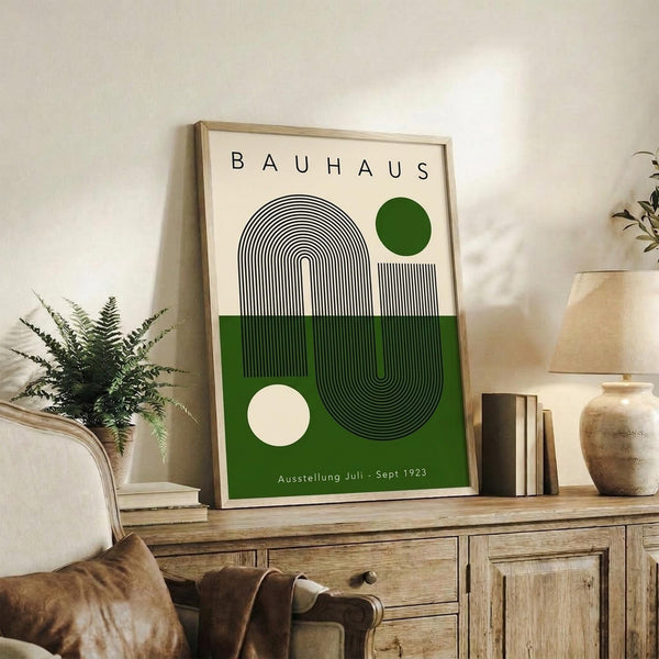 May include: Framed Bauhaus-style poster with geometric black line design and green circle on cream background, displayed on rustic wooden sideboard with books, ceramic vase, and fern plant in modern living room setting with beige armchair and neutral wall
