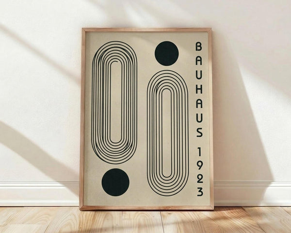 May include: Framed geometric poster with cream background featuring black line art of curved rectangular shapes and two dark green circles, displayed on light wood floor against white wall with natural lighting and shadows