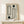 May include: Framed poster with geometric black line art featuring concentric oval and rectangular shapes, two solid black circles, and vertical text reading "BAUHAUS 1923" on cream background. Natural wood frame sits on light wooden surface next to small white wrapped gift with greenery. Clean minimalist room setting with white walls.