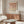May include: Framed geometric poster with terracotta, beige, and cream circles and semicircles arranged in a grid pattern, displayed on wooden sideboard in modern living room with white chair, glass coffee table, and floor lamp