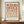 May include: Framed geometric poster with earth-toned circles and semicircles arranged in a grid pattern, featuring warm rust, terracotta, and beige colors on cream background. Text reads "BAUHAUS 1923" at bottom. Displayed on wooden sideboard with small white ceramic vase and stacked books in elegant room with white paneled walls.