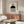 May include: Minimalist Bauhaus exhibition poster with geometric black circle, striped rectangle, and spiral design elements displayed above a wooden sideboard in modern living room setting with cream chair, glass coffee table, white lamp, and wall clock creating contemporary home decor scene