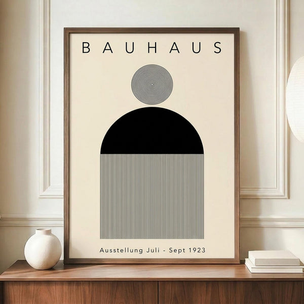 May include: Framed Bauhaus-style poster with geometric black semicircle, concentric circle pattern, and vertical black and white stripes on cream background. Displayed on wooden sideboard next to white ceramic vase and books in elegant room with white paneled walls.