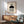 May include: Geometric Bauhaus-style poster with abstract shapes including black semicircle, striped rectangle, and concentric circle design, displayed in wooden frame above mid-century modern credenza with ceramic lamp, next to sage green upholstered armchair in bright, minimalist room with white walls and natural lighting casting plant shadows.
