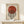 May include: Framed Bauhaus exhibition poster with red circle overlapping black and white striped circle on cream background, displayed on light wood console table next to small wrapped gift with twine and greenery sprig against white wall