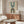 May include: Framed geometric poster with blue and brown arched shapes on cream background, displayed above walnut credenza in modern living room. White curved chair and glass coffee table visible. Warm natural lighting creates shadows on white walls.