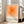 May include: Framed poster with white frame leaning against light gray wall next to beige sofa. Artwork features concentric orange squares in gradient tones from deep orange center to pale peach edges. Black text below reads "bauhaus-archiv" with smaller German text underneath. Bright natural light streams through windows onto hardwood floors with area rug.