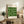 May include: Framed Bauhaus exhibition poster with green geometric circles and semi-circles on cream background, displayed on rustic wooden sideboard alongside fern plant, books, and ceramic vases in warm neutral living room setting