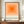 May include: Framed poster with concentric orange squares in gradient shades from deep orange center to pale peach, displayed on wooden sideboard next to white ceramic vase and books. Black text reads "bauhaus-archiv" with German museum details below. Warm beige walls with white molding visible in background.