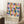 May include: Framed geometric art print with colorful overlapping circles in pink, blue, orange, and yellow tones on cream background, leaning against white wall next to wooden side table with coffee cup, placed on textured white rug with cozy knit blanket nearby in soft natural lighting.