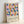 May include: Framed poster with geometric pattern of colorful overlapping circles in blue, pink, orange, yellow and coral tones arranged in a grid. Text reads "bauhaus-archiv" with smaller German text below. Light wooden frame against white wall, natural lighting casting soft shadows.