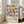May include: Framed geometric art print leaning against white wall beside beige sofa in bright living room. Colorful poster features overlapping circles and squares in pink, blue, orange, and yellow arranged in grid pattern. Black text below reads "bauhaus-archiv" with museum details. Natural wood frame, hardwood floors, large windows with natural lighting.