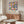 May include: Modern living room with walnut credenza displaying colorful geometric Bauhaus poster featuring overlapping circles in pink, blue, orange, and green. Cream upholstered chair, brass floor lamp, and oval glass coffee table complete the mid-century inspired space with white walls and natural lighting.
