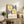 May include: Framed Bauhaus-style poster with geometric semicircles in yellow and black concentric lines on cream background, displayed on rustic wooden sideboard alongside fern plant, books, ceramic vase, and brown leather chair in warm neutral living room setting