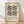 May include: Framed geometric poster with black triangular and circular shapes arranged in symmetrical pattern on cream background, displayed against white wall on light wooden floor with natural shadows