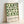 Framed poster featuring geometric pattern of white circles on forest green background with black text reading "bauhaus-archiv" and "museum für gestaltung klingelhofstrasse, berlin" below. Light wood frame leaning against white wall, casting subtle shadow.