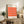 May include: Framed Bauhaus exhibition poster with geometric orange and pink cube pattern displayed on rustic wood sideboard in modern living room setting, surrounded by fern plant, ceramic vase, stacked books, and beige upholstered chair with leather cushion