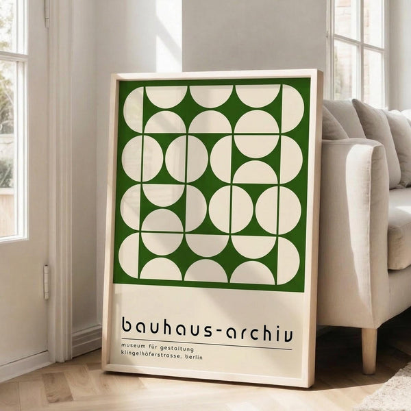 May include: Framed poster with geometric green and cream circular pattern leaning against white wall next to beige sofa in bright living room with hardwood floors and large windows. Light wood frame contains modernist design with repeating circles arranged in grid formation above black text on cream background.