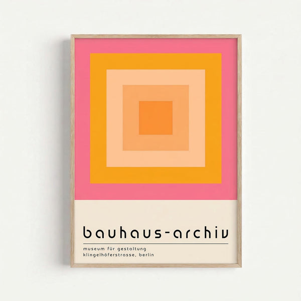Framed geometric art print featuring concentric squares in gradient shades of pink, orange, and peach tones. The minimalist design shows nested squares creating depth through color transition from bright coral pink border to deep orange center. Below the artwork is text reading "bauhaus-archiv" and "museum für gestaltung klingelhöferstrasse, berlin" in modern sans-serif typography on cream background. Light wood frame against white wall.