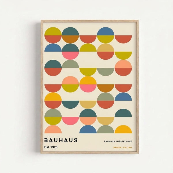 Framed geometric art print featuring colorful semi-circles and circles arranged in rows. The design uses vibrant colors including yellow, orange, coral, teal, blue, pink, and olive green against a cream background. Text at bottom reads "BAUHAUS Est 1923" and "BAUHAUS AUSSTELLUNG WEIMAR JULI 1923". The print is displayed in a light wood frame against a white wall, showing the modern minimalist Bauhaus design style with bold geometric shapes.